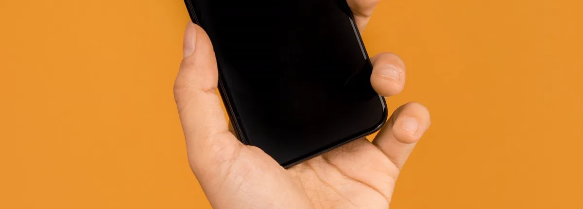 Hand hält ein Telefon vor orangefarbenem Hintergrund